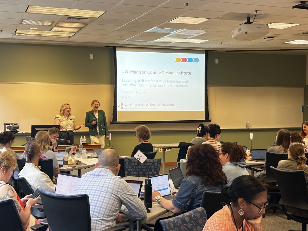 Emily Hall and Abby Letak present to a room of people seated at rectangular tables