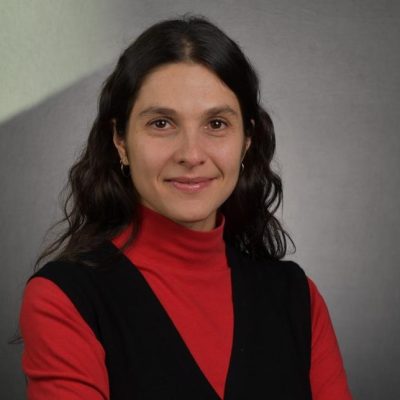 Antonella is wearing a red turtleneck and a black vest.
