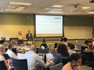 Emily Hall and Abby Letak present to a room of people seated at rectangular tables
