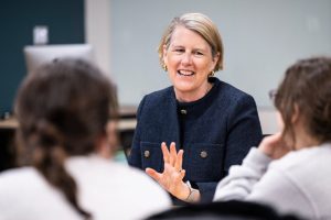 Emily Hall sitting and talking with two students while teaching